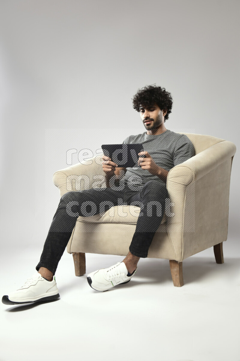 A man wearing casual sitting on a chair gaming on a tablet on white background