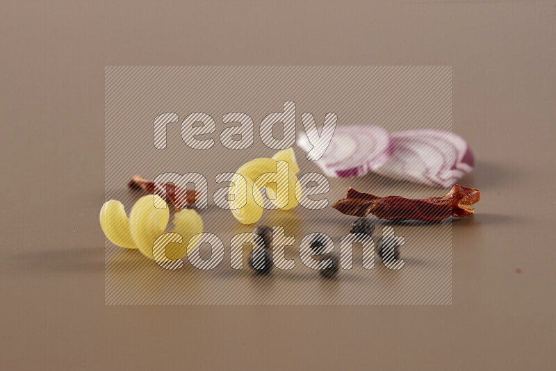 Raw pasta with different ingredients such as cherry tomatoes, garlic, onions, red chilis, black pepper, white pepper, bay laurel leaves, rosemary and cardamom on beige background