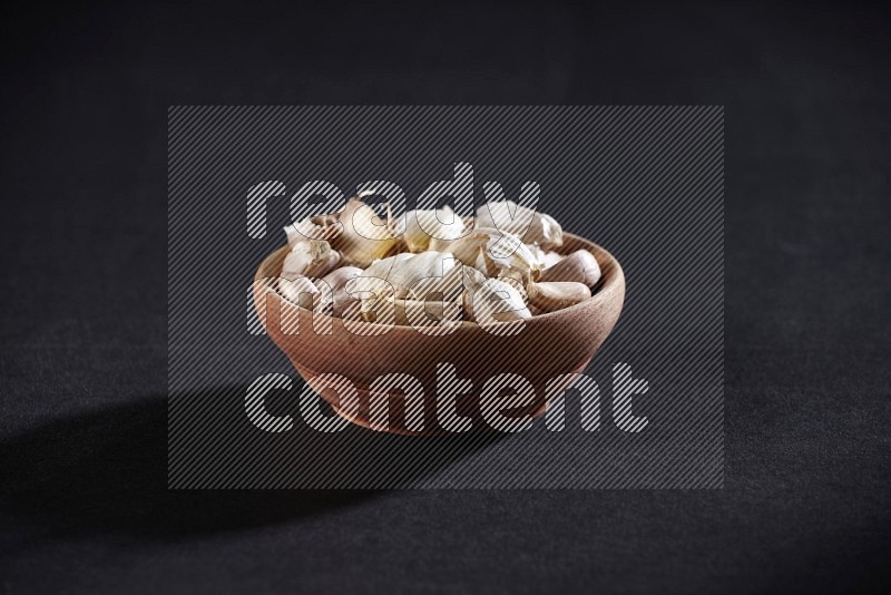 A wooden bowl full of garlic cloves on a black flooring in different angles