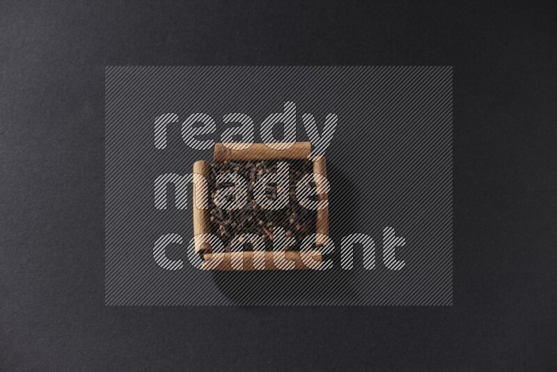 A single square of cinnamon sticks full of cloves on black flooring