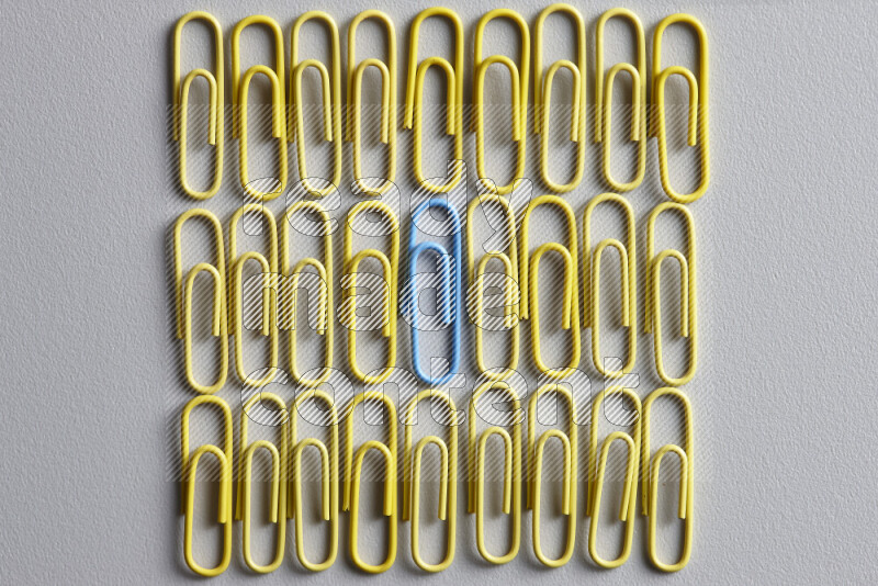 A bunch of yellow paper clips with a different colored paper clip in the center on grey background