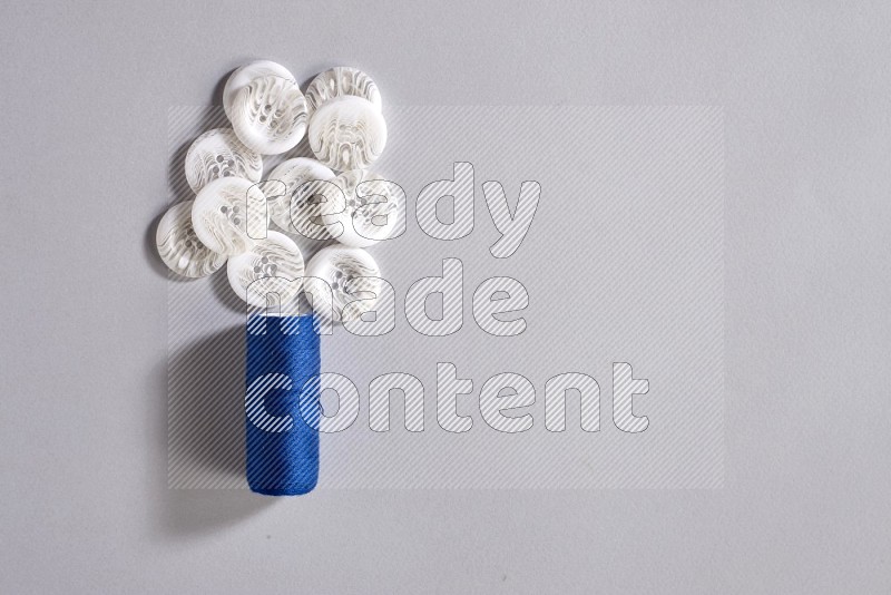 A blue sewing thread spool with colored buttons on grey background