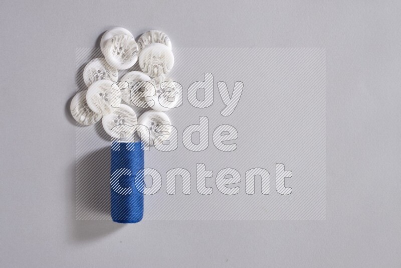A blue sewing thread spool with colored buttons on grey background