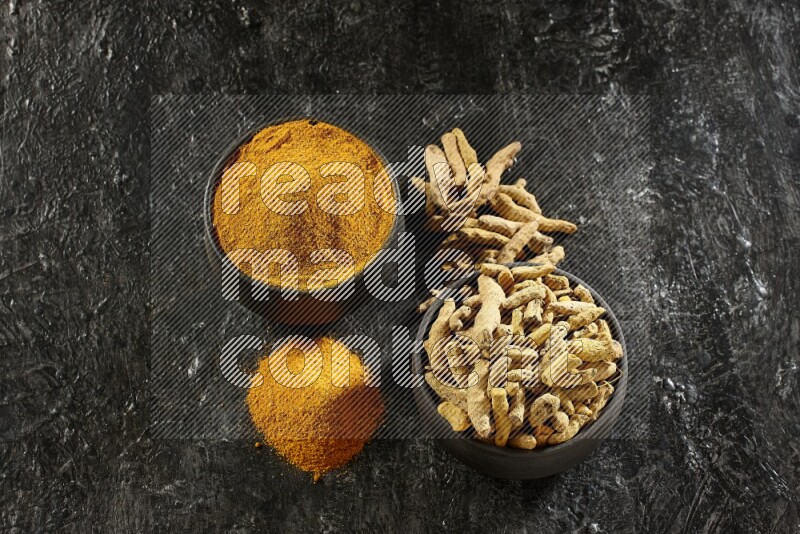 وعاءان من الفخار باللون الأسود، أحدهما ممتلئ ببودرة الكركم والآخر ممتلئ بأصابع كاملة من الكركم المجفف على خلفية سوداء