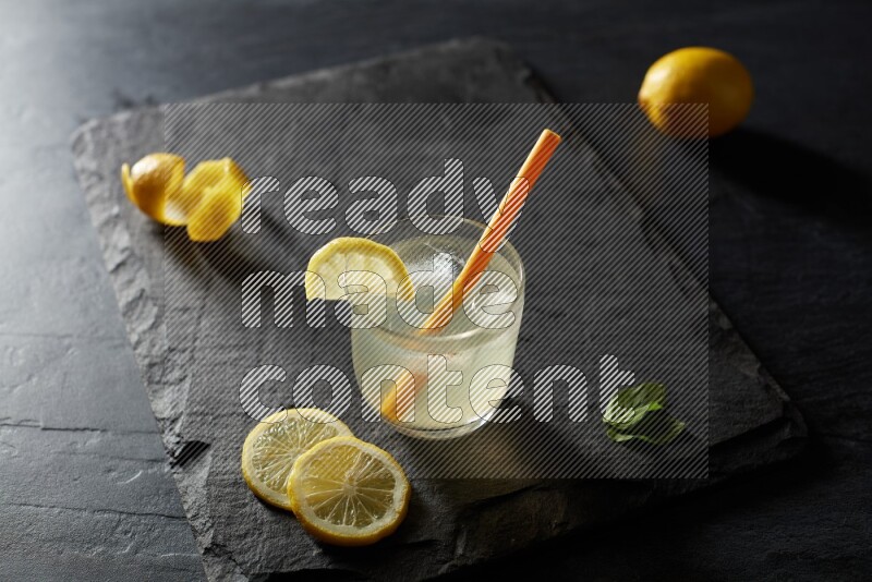 A glass of lemon juice with a straw on black background