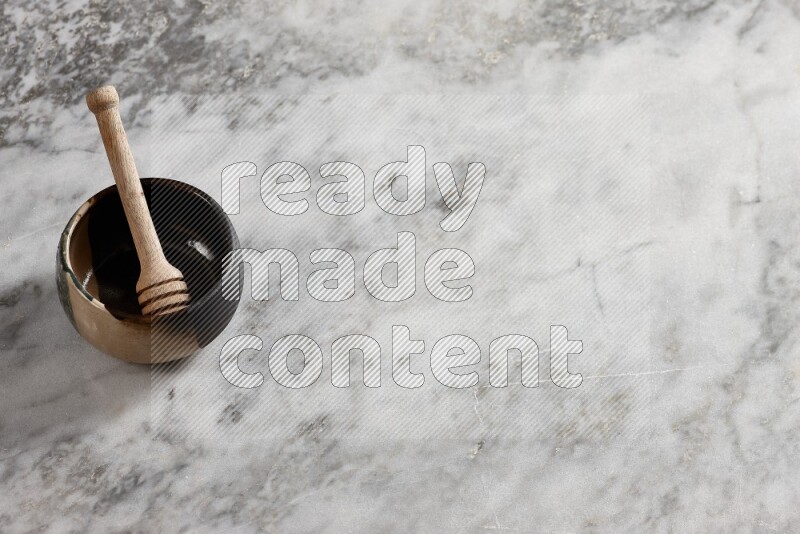 Multicolored pottery bowl with wooden honey dipper in it on grey marble background