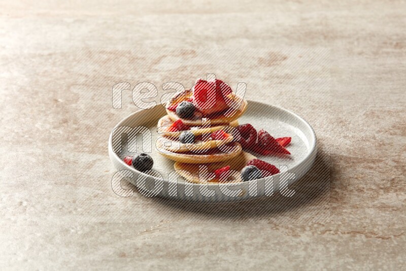 Five stacked mixed berries mini pancakes in a blue plate on beige background