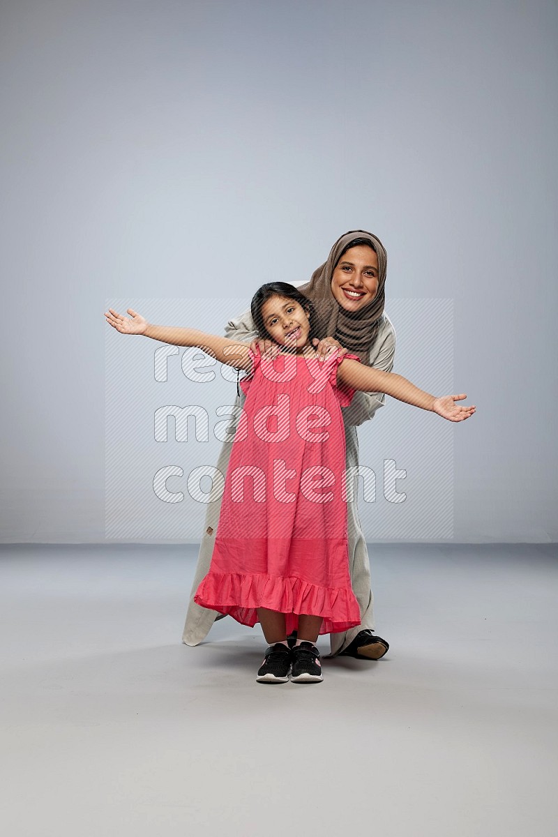 A girl and her mother interacting with the camera on gray background