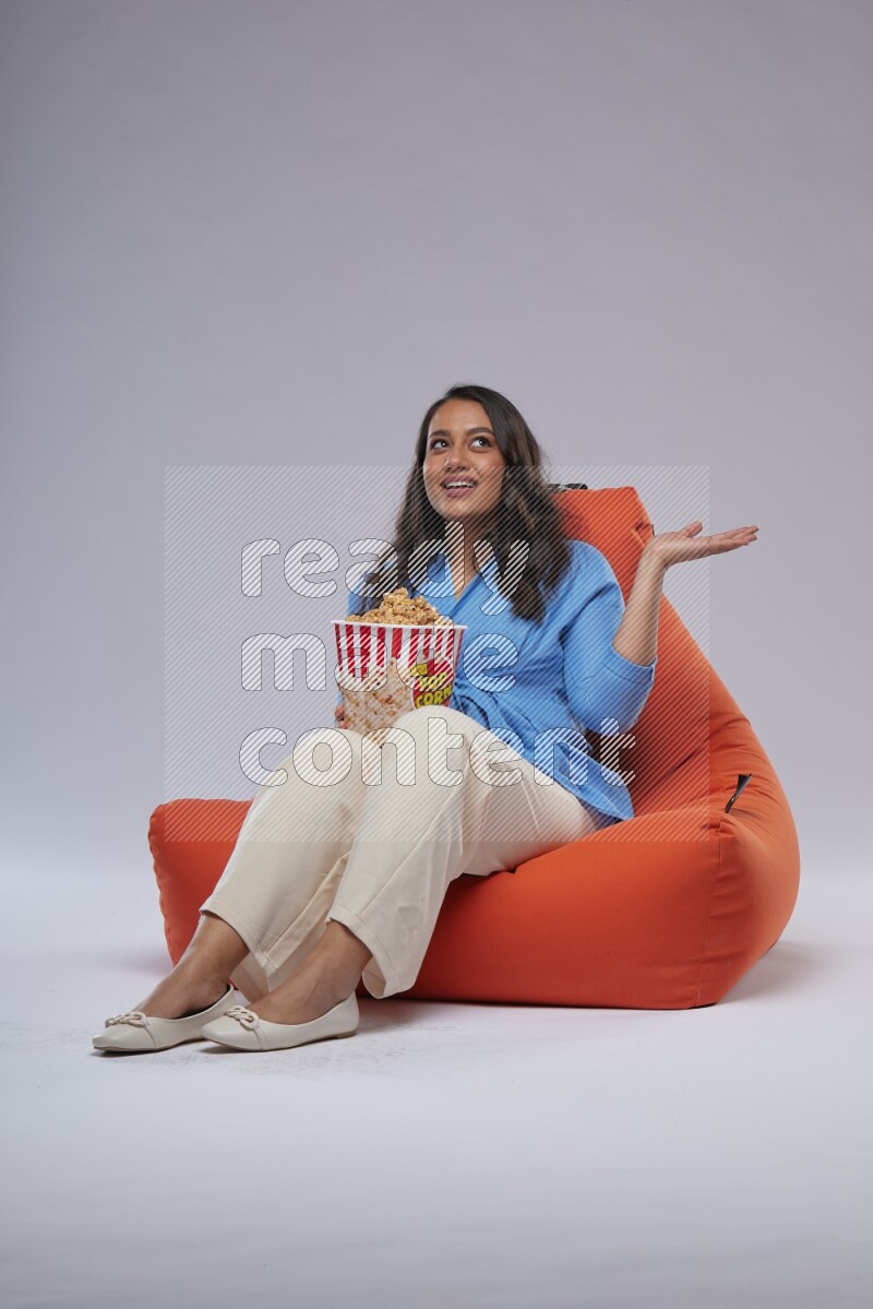 A woman sitting on an orange beanbag and eating popcorn