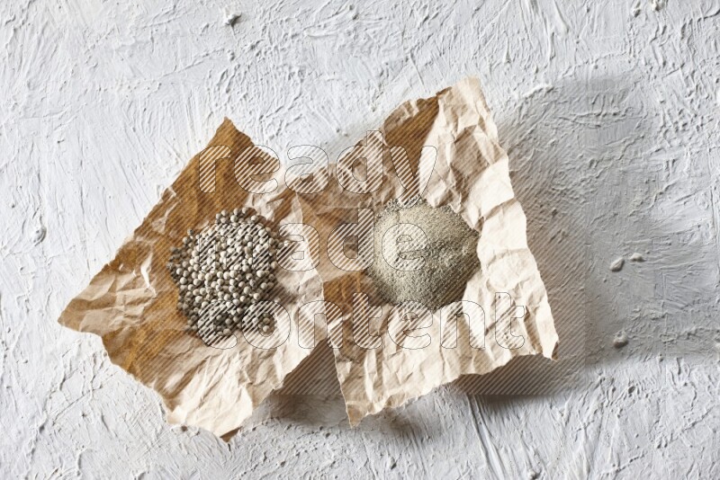 White pepper beads and powder in crumpled pieces of paper on textured white flooring