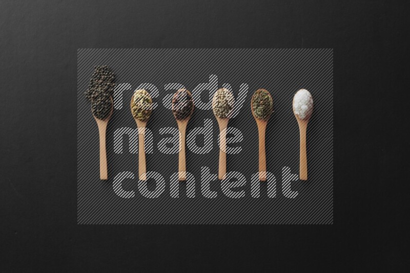 الفلفل الأبيض والقرنفل والهيل والملح والفلفل الأسود وريحان مجفف في معالق خشبية علي خلفية سوداء