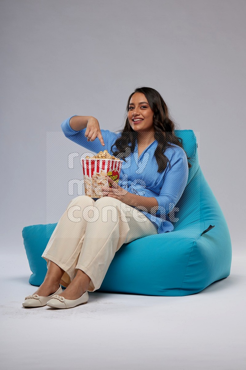 A woman sitting on a blue beanbag and eating popcorn