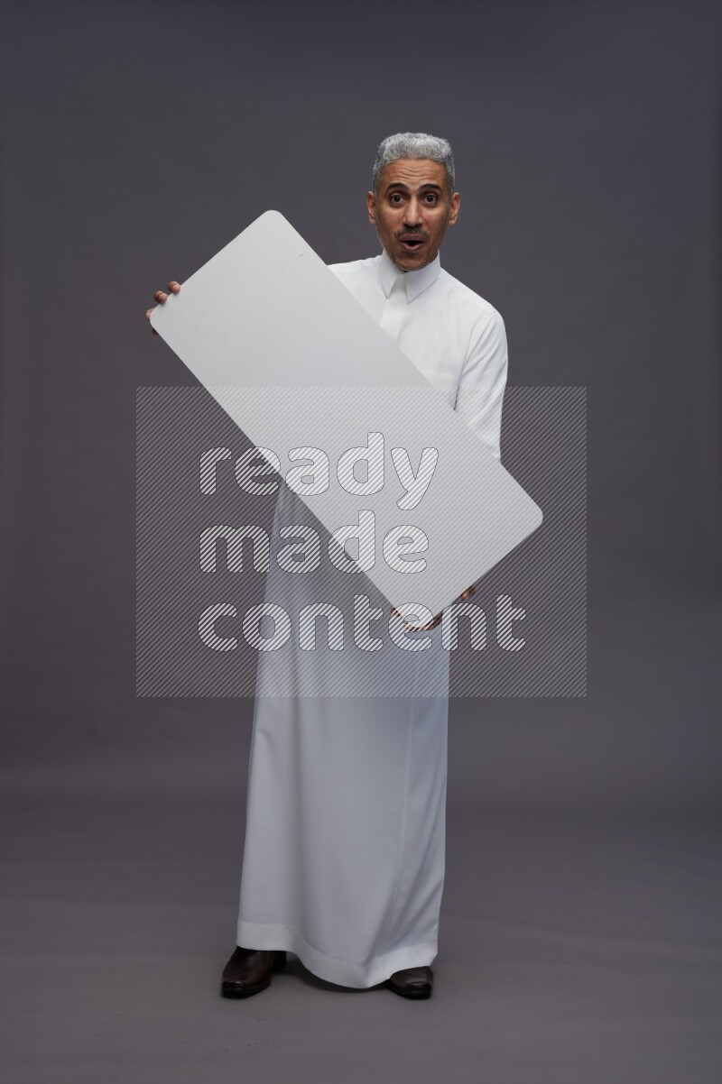 Saudi man wearing thob standing holding board on gray background