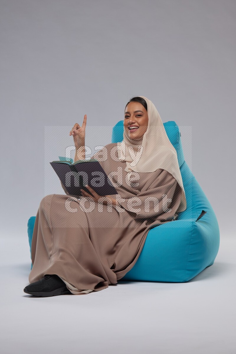 A woman sitting on a blue beanbag and reading a book