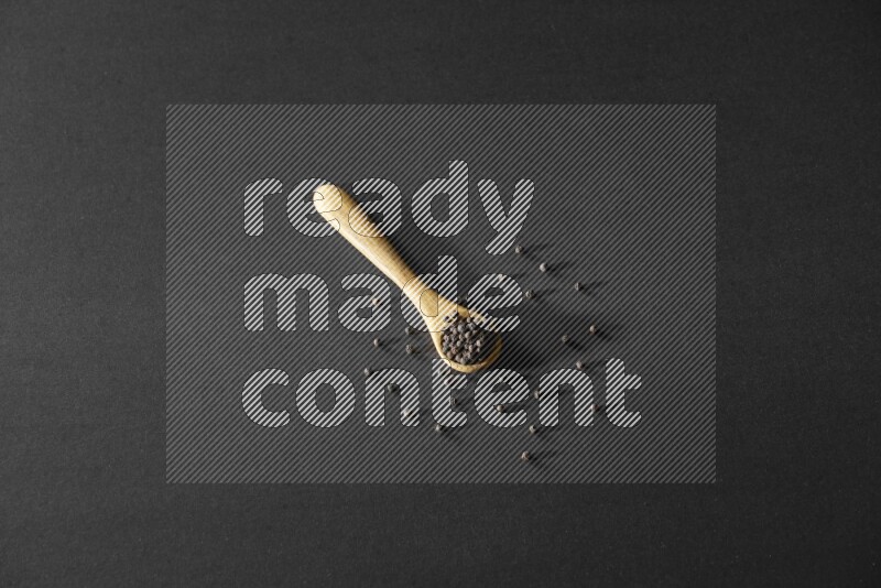 حبوب الفلفل الأسود في ملعقة خشبية علي خلفية سوداء