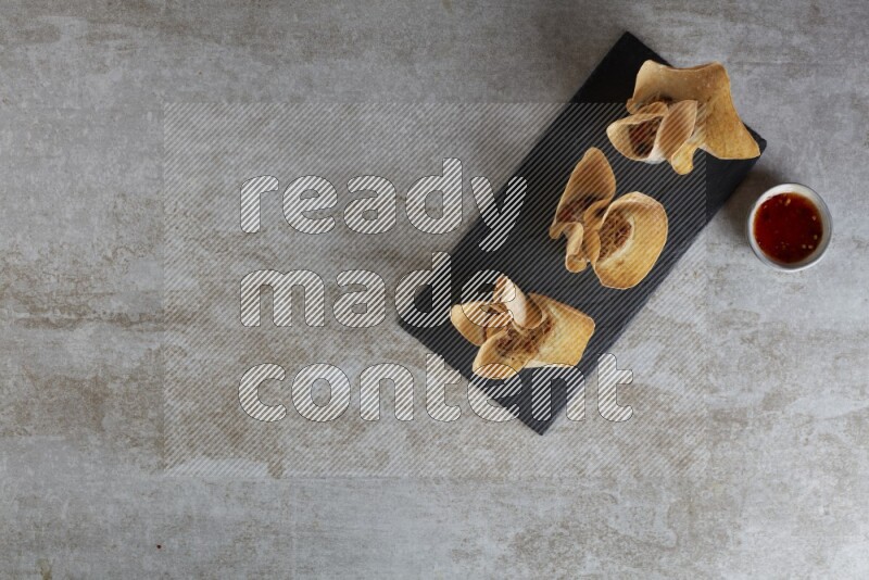 wonton cups with soy sauce ramkin on rectangle slate on grey textured counter top