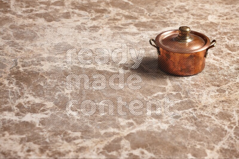 A small copper pot on beige marble background