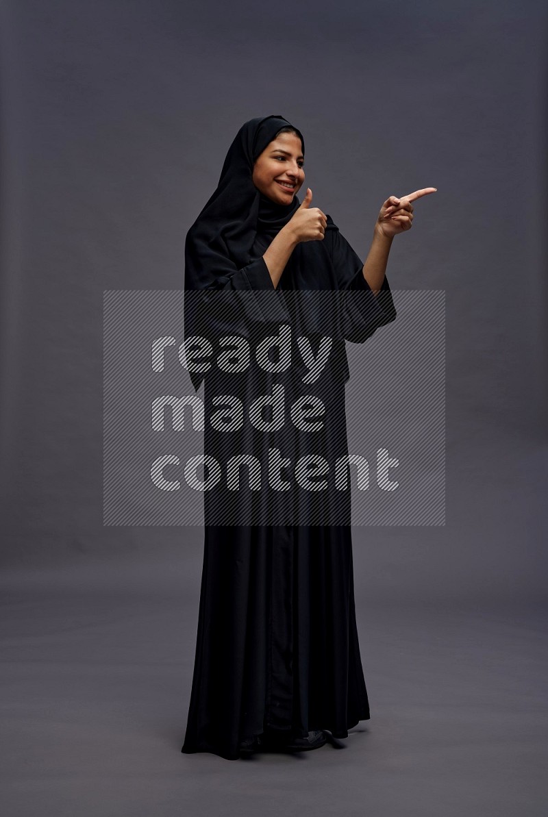 Saudi woman wearing Abaya standing interacting with the camera on gray background