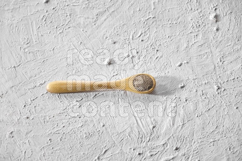 A wooden spoon full of black pepper powder on a textured white flooring