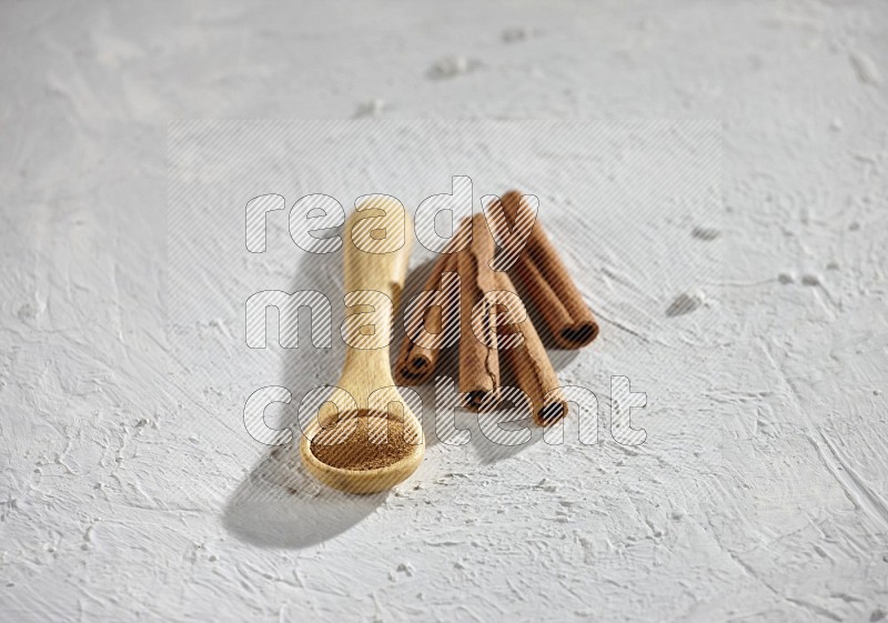 Cinnamon powder in a wooden spoon with cinnamon sticks on white background