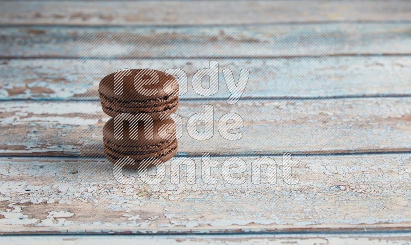 45º Shot of two Brown Dark Chocolate macarons on light blue wooden background