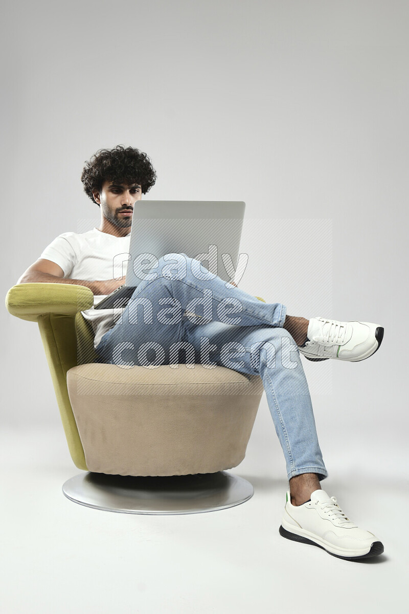 رجل يرتدي ملابس كاجوال يجلس علي كرسي و يعمل علي لاب توب علي خلفية بيضاء