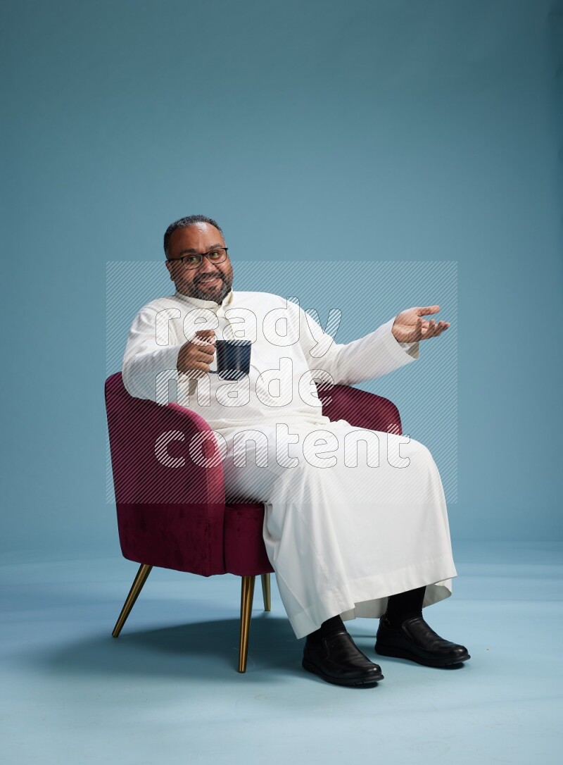 Saudi Man without shimag sitting on chair drinking coffee on blue background