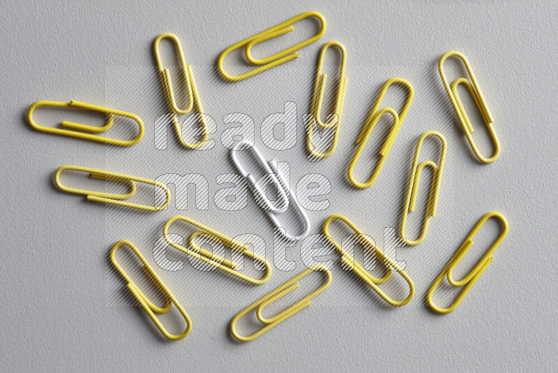 A bunch of yellow paper clips with a different colored paper clip in the center on grey background