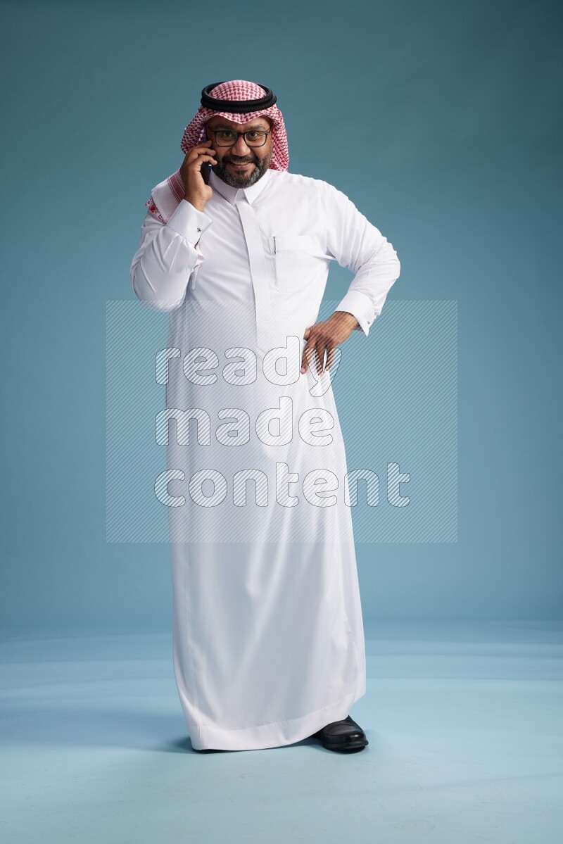 Saudi Man with shimag Standing talking on phone on blue background