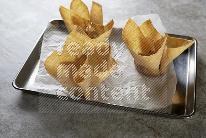 wonton cups on parchment paper in stainless tray on grey textured counter top