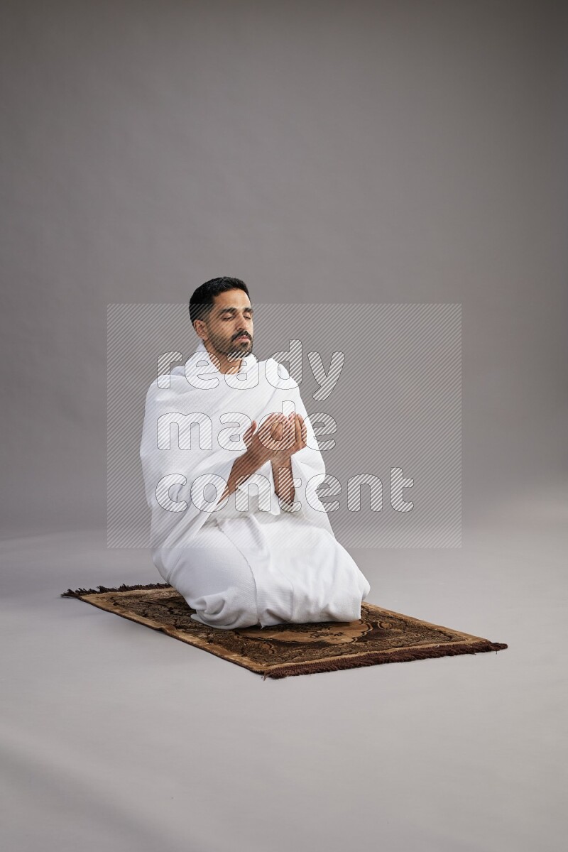 A man wearing Ehram performing dua'a on gray background
