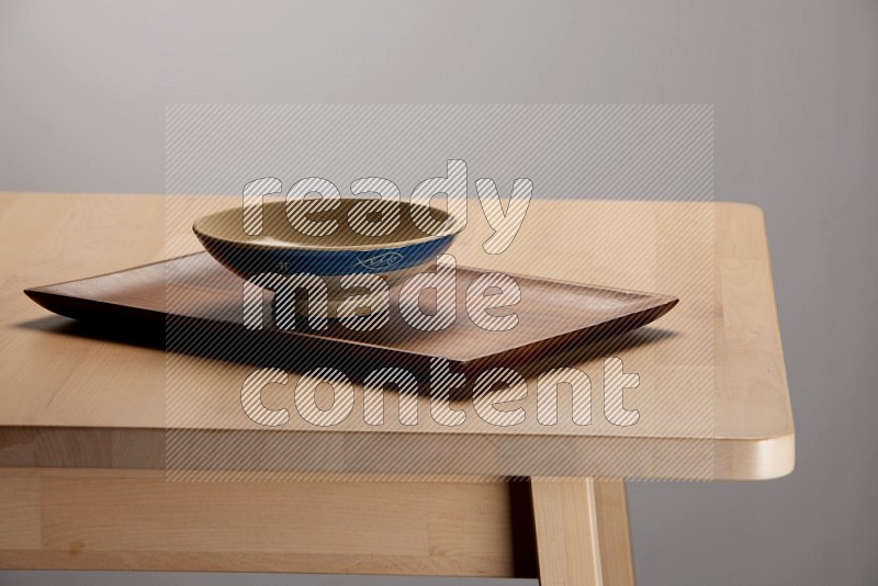 multicolored bowl placed on a rectangular wooden tray on the edge of wooden table