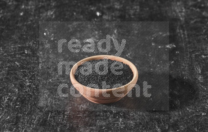 A wooden bowl full of black seeds on a textured black flooring