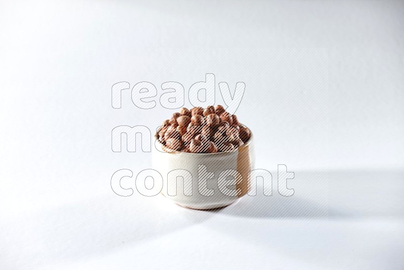 A beige ceramic bowl full of peeled hazelnuts on a white background in different angles