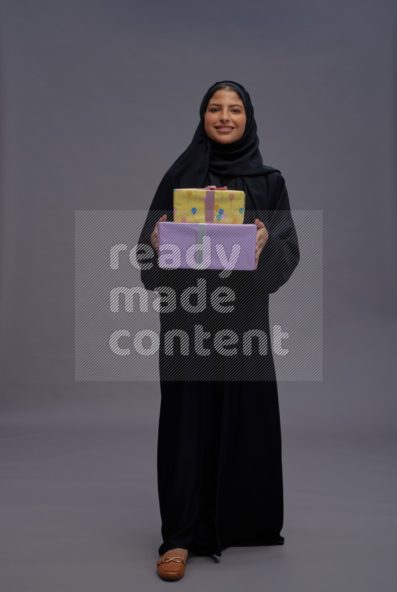 Saudi woman wearing Abaya standing holding gift box on gray background