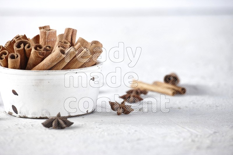 White bowl full of cinnamon sticks surrounded by star anis on a textured white background in different angles