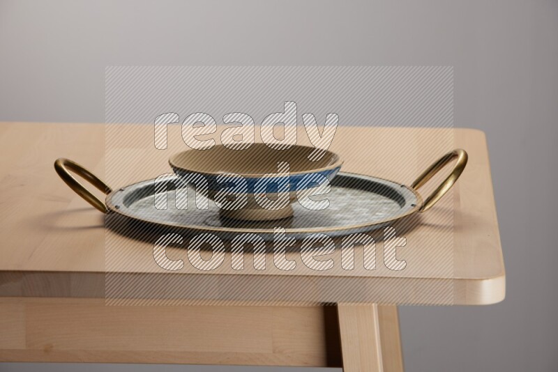 multicolored bowl placed on a rounded stainless steel tray with golden handels on the edge of wooden table