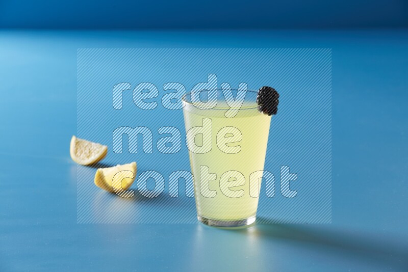 glass of lemon juice with berry on blue background