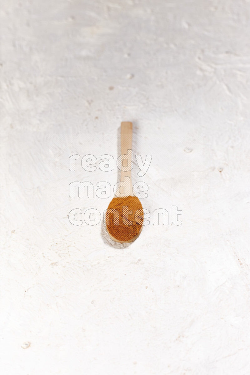 A wooden spoon full of ground paprika powder on white background