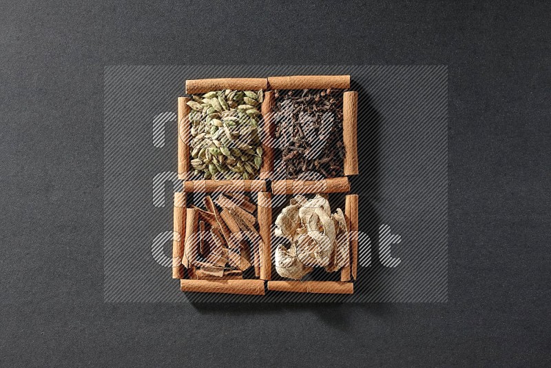 4 مربعات من عيدان القرفة ممتلئة بقطع القرفة وحبوب الهيل والقرنفل والزنجبيل المجفف على أرضية سوداء
