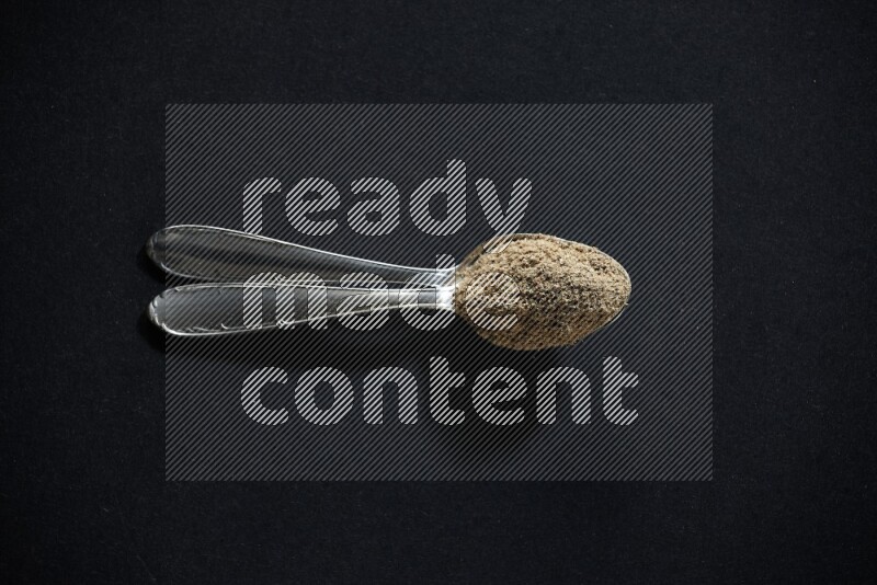 ملعقتان معدنيتان ممتلئتان ببودرة الهيل على خلفية سوداء