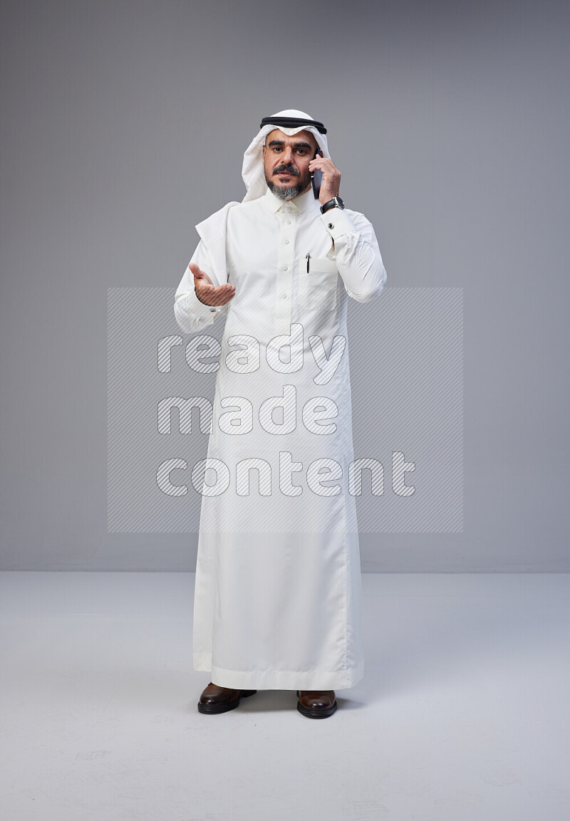 Saudi man Wearing Thob and white Shomag standing talking on phone on Gray background