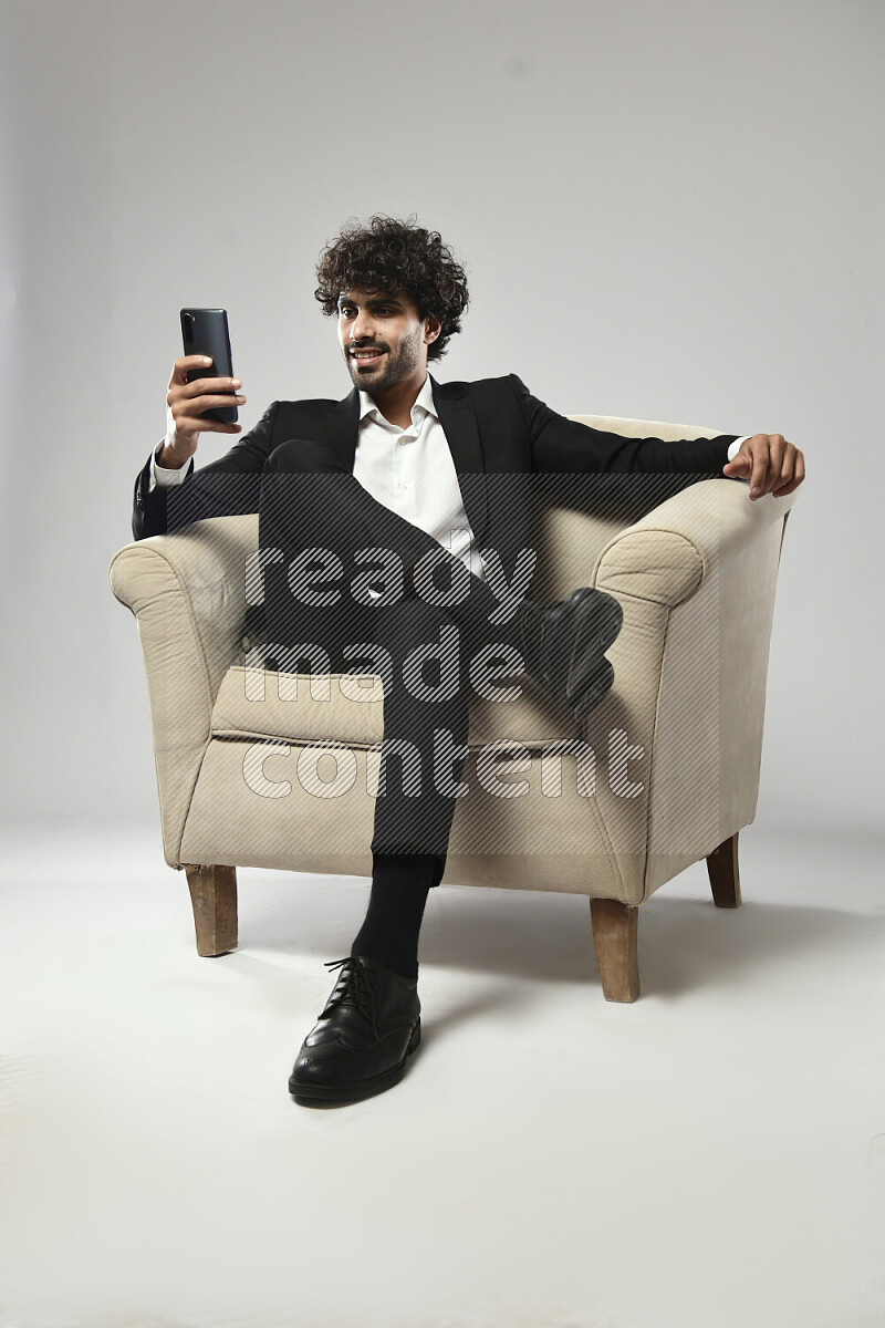 رجل يرتدي ملابس رسمية يجلس علي كرسي و يرسل رسائل نصية علي الهاتف علي خلفية بيضاء