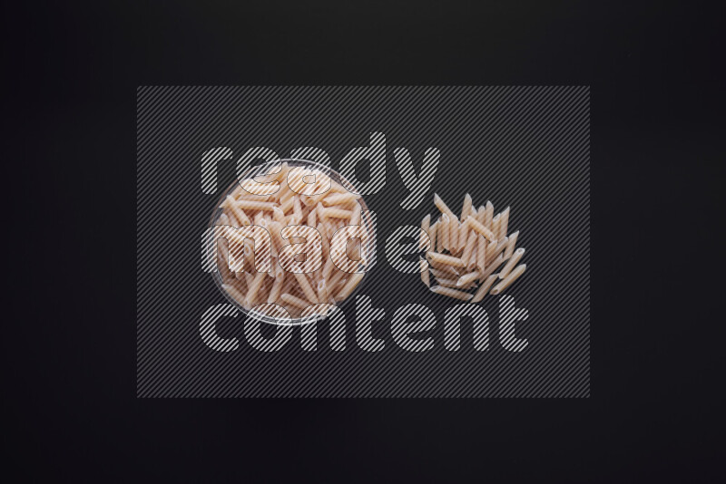 Mini penne pasta in a glass bowl on black background