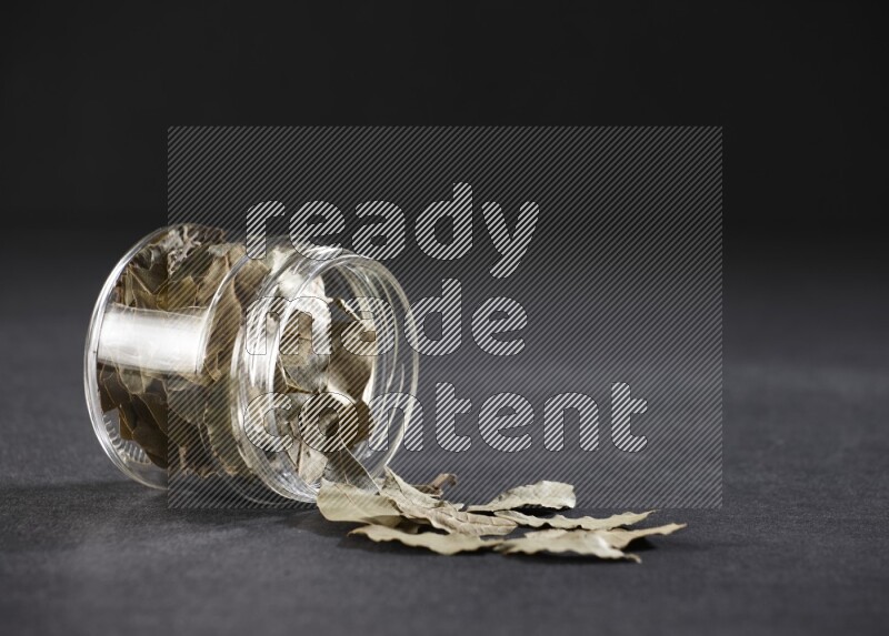 وعاء زجاجي ممتلئ بأوراق الغار والوعاء مقلوب وبعض الأوراق متناثرة خارجه علي خلفية سوداء