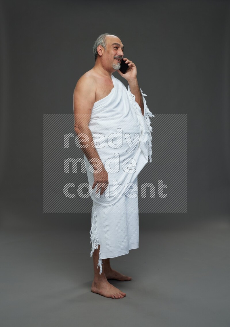 A man wearing Ehram Standing talking on phone on gray background