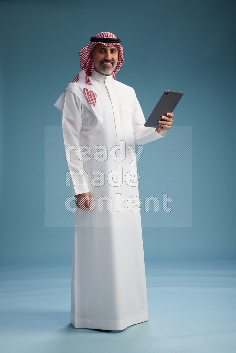 Saudi man wearing thob and shomagh with tablet on Blue background