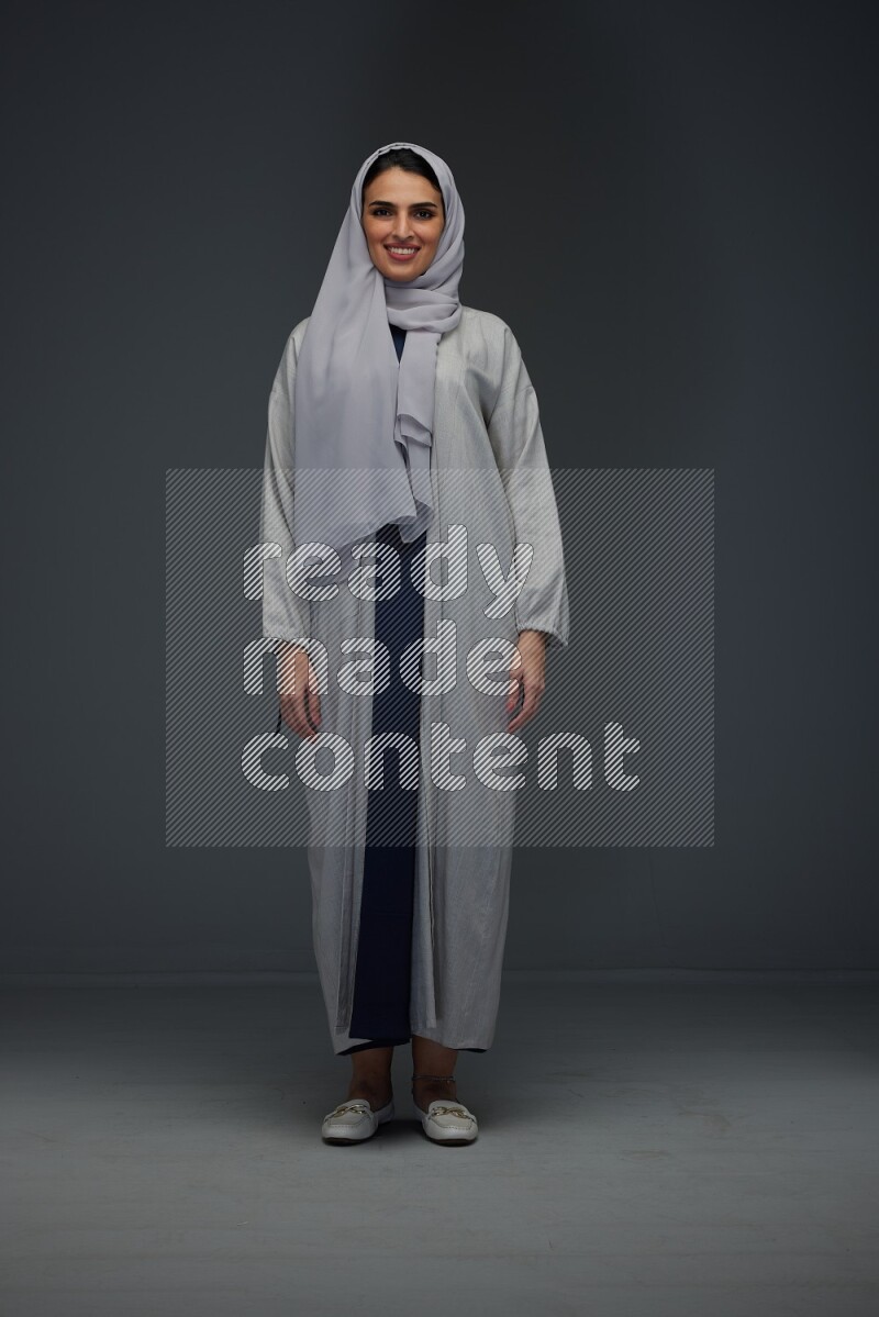A Saudi woman wearing a light gray Abaya and head scarf standing and making multi poses eye level on a grey background