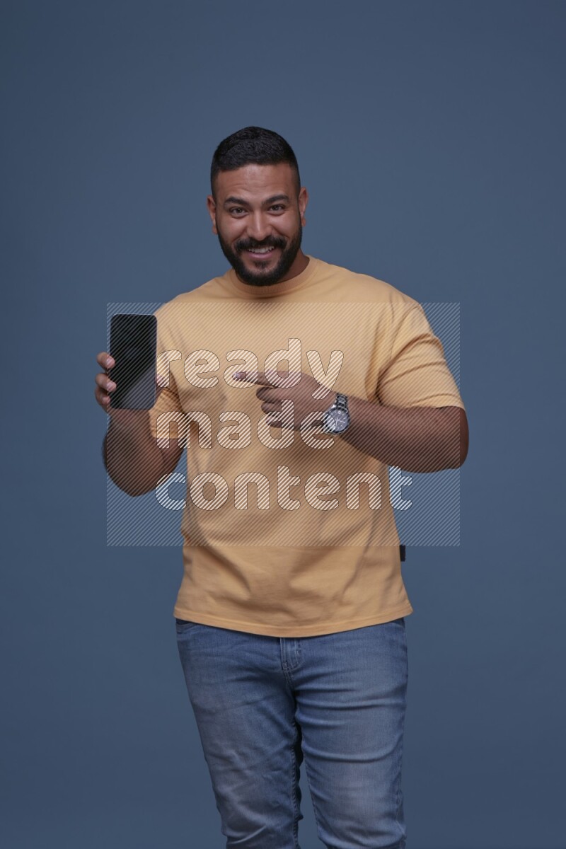 A man Pointing at a Smartphone on Blue Background wearing Orange T-shirt