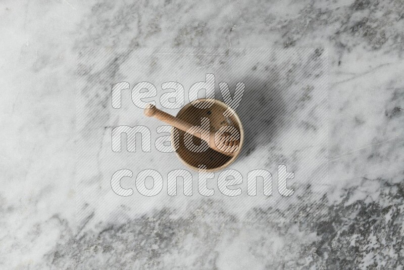 Multicolored pottery bowl with wooden honey dipper in it on grey marble background